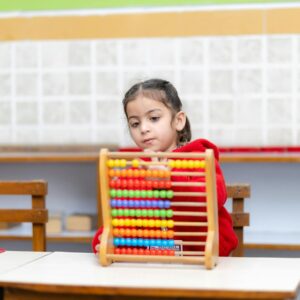 Young child uses colorful abacus in a bright classroom setting.
