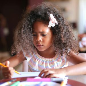 African American child focused on homework, writing with a pencil indoors.