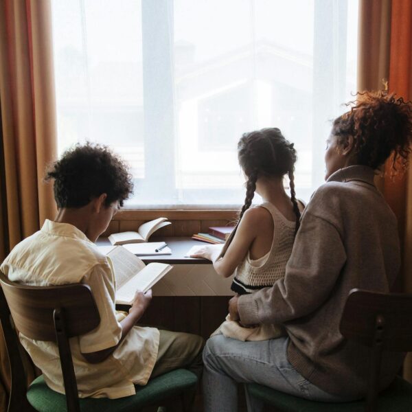 A family of three reads by a window, enjoying a quiet and educational moment indoors.