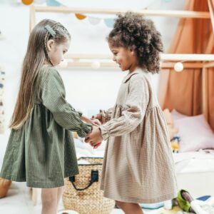Two young girls holding hands and playing indoors, expressing joy and friendship in a cozy playroom.