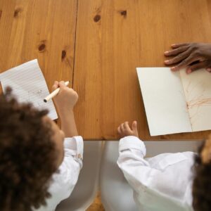 Two kids with curly hair drawing together at a wooden table, enjoying creative time.