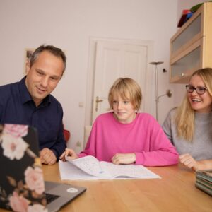 Family engaged in online learning together at home using laptop, focusing on education and connection.