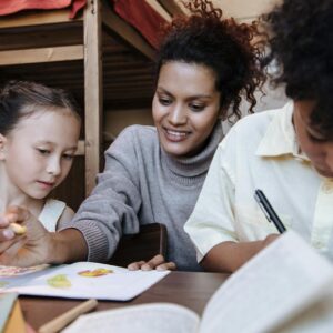 A mother spends quality time with her children, drawing and learning together indoors.