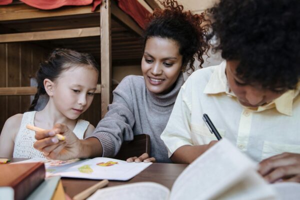 A mother spends quality time with her children, drawing and learning together indoors.